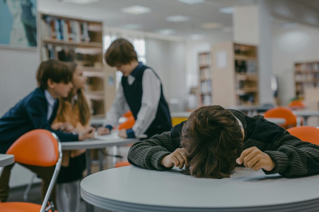 studente - A child sits alone in a school library, highlighting themes of bullying and isolation.